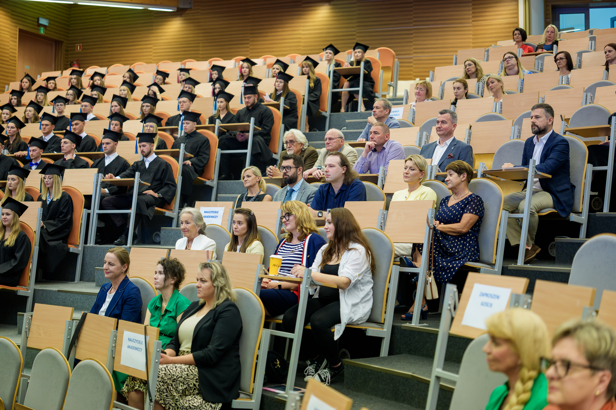 Aula wypełniona absolwentami, rodzinami i ich przyjaciółmi.