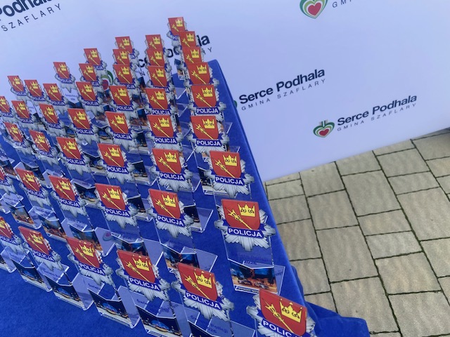Zbliżenie na liczne statuetki z logo Policji oraz herbem, ustawione w rzędach na stole przykrytym niebieskim obrusem. W tle widać ściankę z napisem „Serce Podhala Gmina Szaflary”.