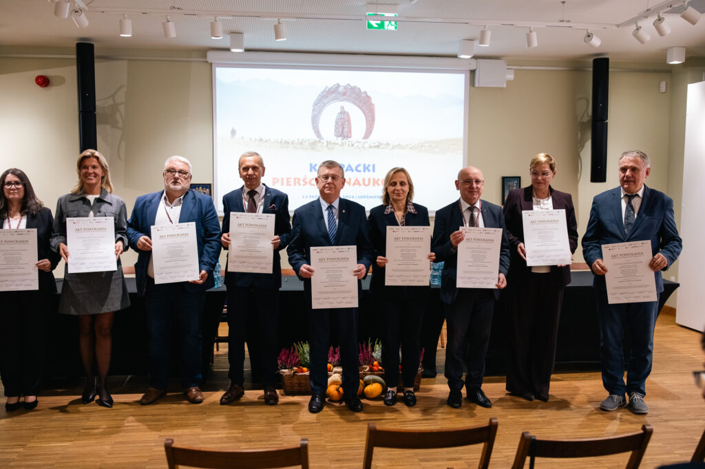 Grupa osób stoi na scenie, prezentując podpisane akty powołania