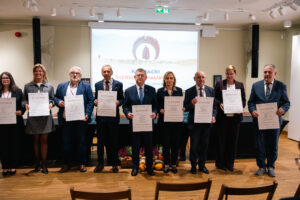 Grupa osób stoi na scenie, prezentując podpisane akty powołania