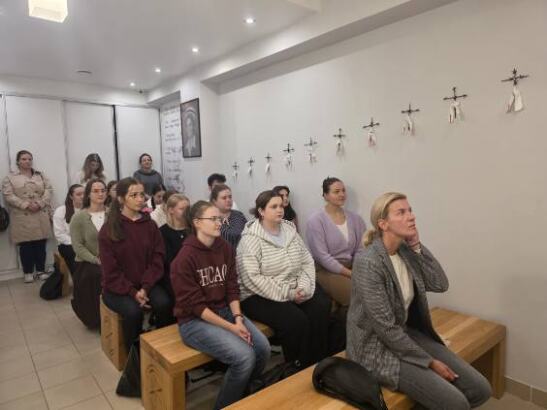 Wierni siedzą na drewnianych ławkach w kaplicy i uczestniczą w liturgii